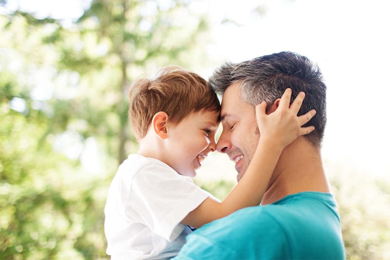 Father and young son touching heads outdoors, sharing a quiet, affectionate moment, symbolising connection and cooperation in shared parenting after separation