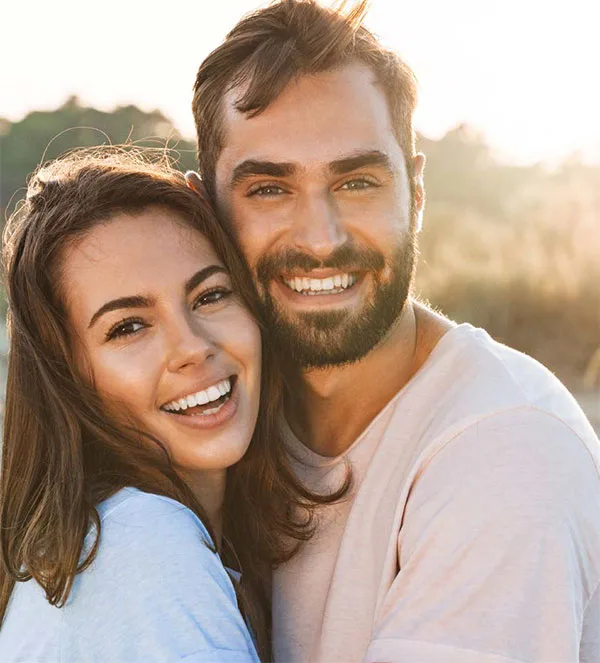 Couple embracing outdoors, looking towards the camera with a warm sun glow behind them, symbolising hope and focused support in relationship distress.