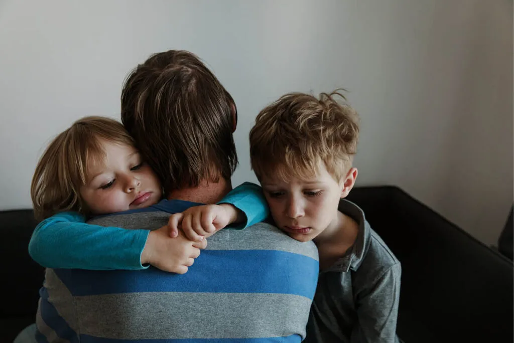 Father hugging his two sons, one with arms around his neck and the other resting his chin on his shoulder—capturing love, family connection, and the emotional weight of relationship decisions.