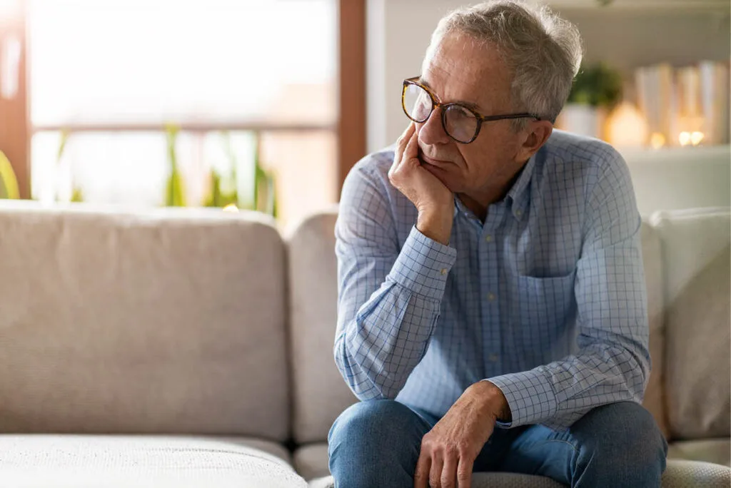 Middle-aged man sitting on a couch with his head resting in his hand, looking contemplative, reflecting on personal challenges and relationships