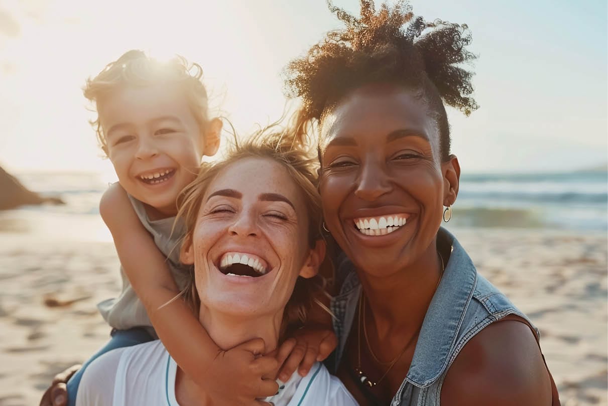 Same-sex couple and their young daughter embracing at the beach in Bali, representing connection and emotional safety. Promotional image for YMU’s Emotionally Focused Family Therapy (EFFT) Essentials training in Bali.